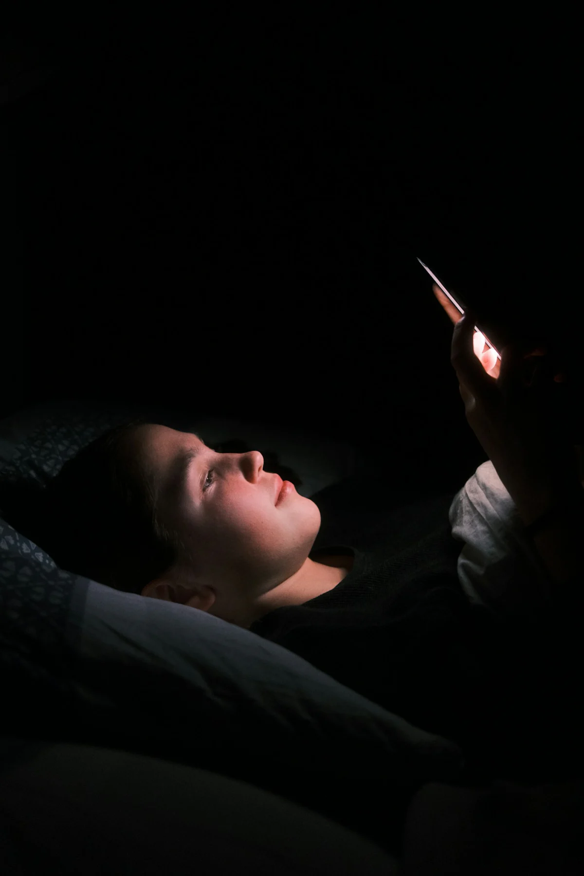 A woman lying in bed at night, her face lit by her phone